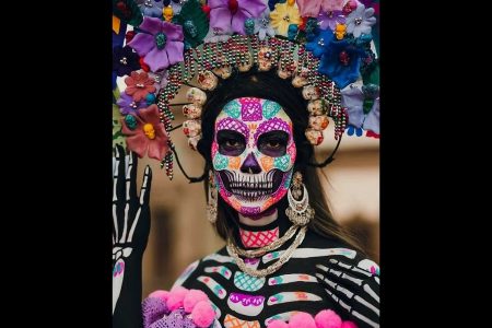 Mujer con un maquillaje de Catrina moderno y colorido para el Día de Muertos, con un tocado de flores y calaveras. Esta es una interpretación artística del ícono mexicano.