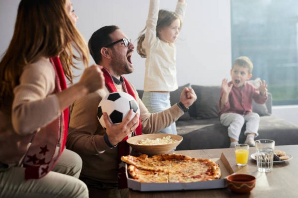 Familia mexicana celebrando un gol con pizza y botanas, mostrando cómo la comida se convierte en una cábala importante durante los partidos del Mundial.
