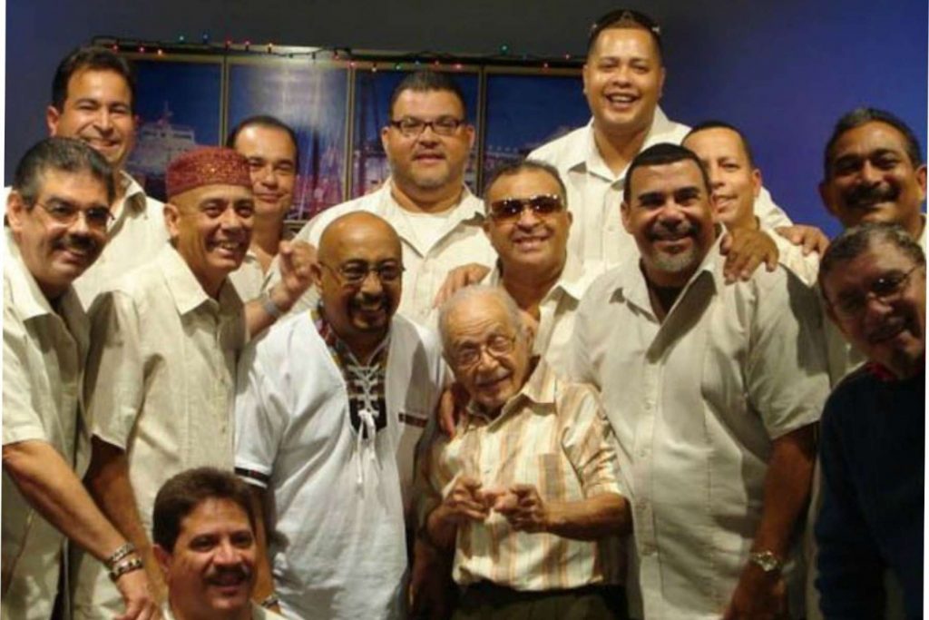 El fundador de La Sonora Ponceña, Don Quique Lucca, rodeado por los músicos de la orquesta. Una imagen que representa el legado y la herencia familiar de una de las instituciones de la salsa.