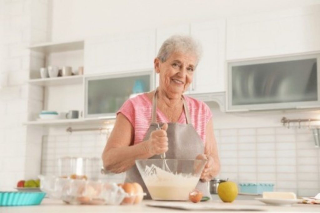 Una abuela sonriente cocinando en su cocina, representando la analogía del portero que protege la portería como la abuela protege su cocina en una fiesta familiar.