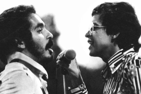 Willie Colón y Héctor Lavoe compartiendo micrófono durante una presentación de salsa en vivo.