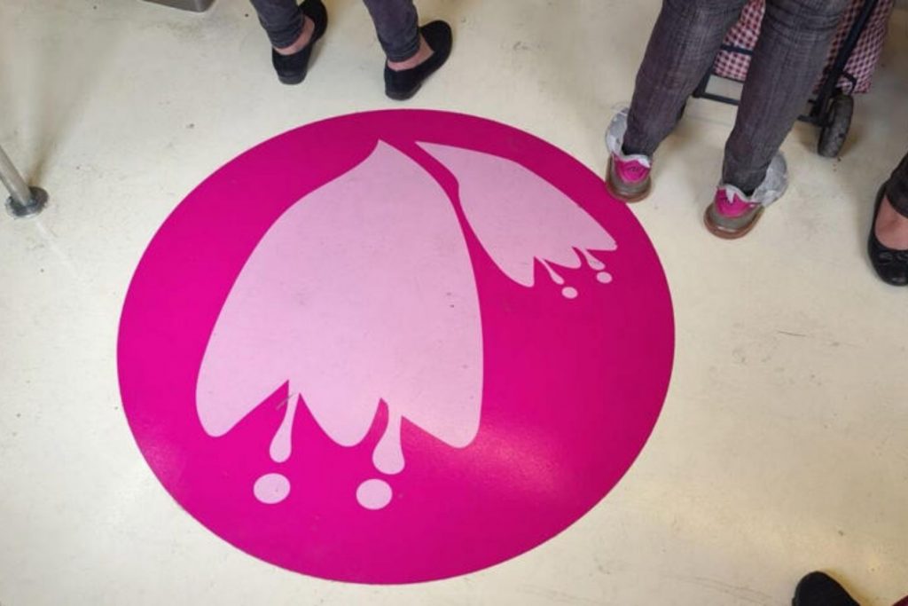 Pegatina circular de color rosa con la silueta de una flor blanca en el piso de un vagón del Metro de la Ciudad de México.