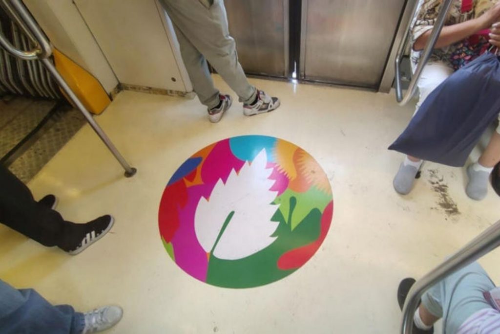 Perspectiva del interior de un vagón del Metro con una pegatina circular multicolor en el pasillo central que muestra un sol o flor blanca.