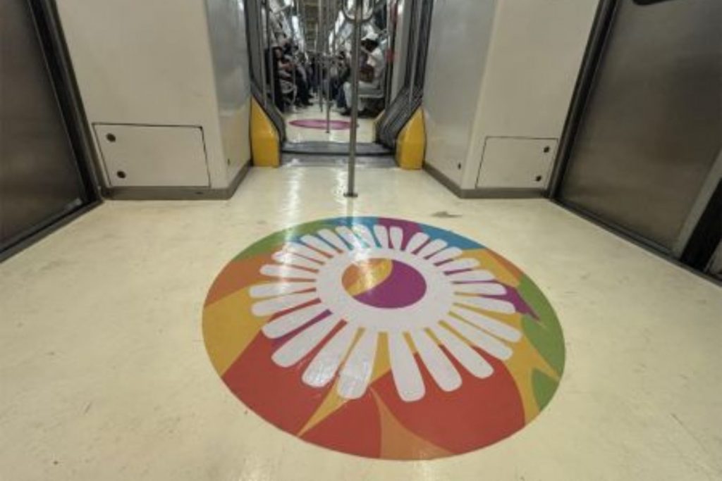 Diseño circular con fondo de diversos colores y una hoja blanca en el centro, pegado en el piso de un vagón del Sistema de Transporte Colectivo Metro.
